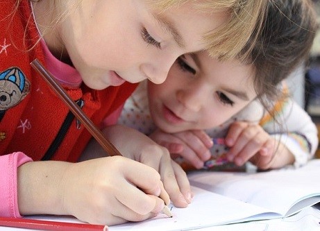 deux enfants assis a un bureau, reflechissant ensemble a un exercice dans un cadre detendu et bienveillant