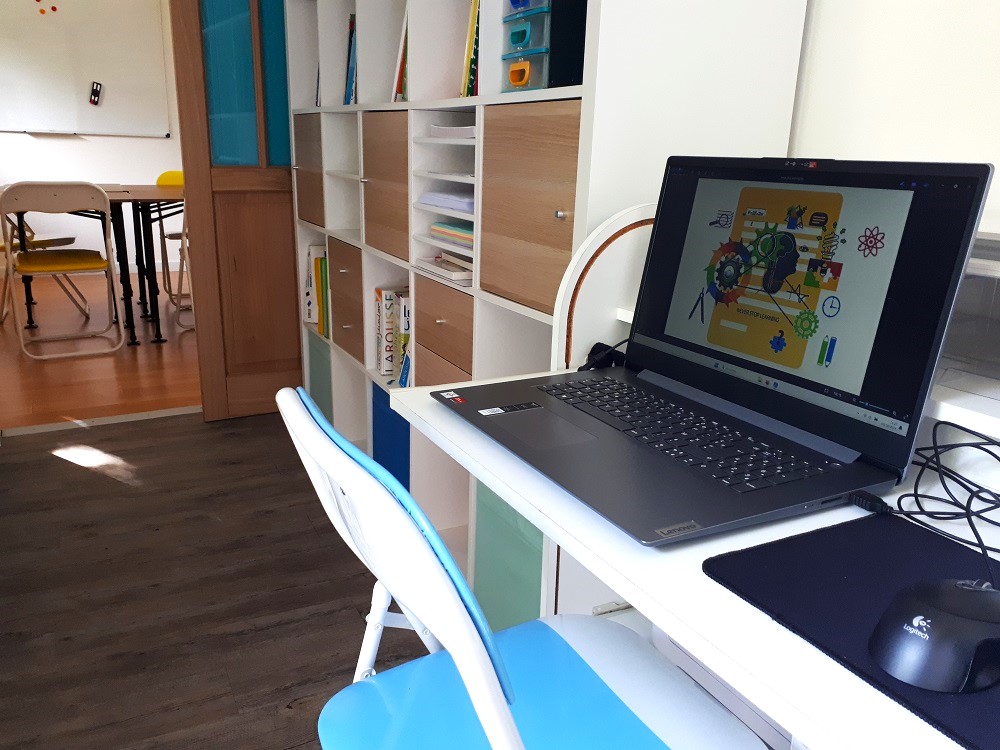 ordinateur pose sur un bureau blanc dans la salle au mur bleu, offrant un espace de travail complementaire aux eleves