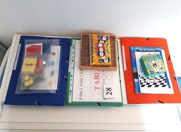 pile de materiel pedagogique preparee pour chaque eleve avec dossier, jeux, cartes plastifiees